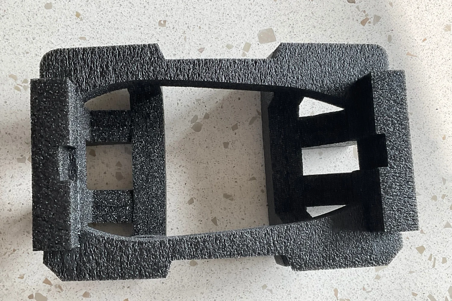 A black foam packaging container with multiple cutouts designed to fit and protect a specific item.