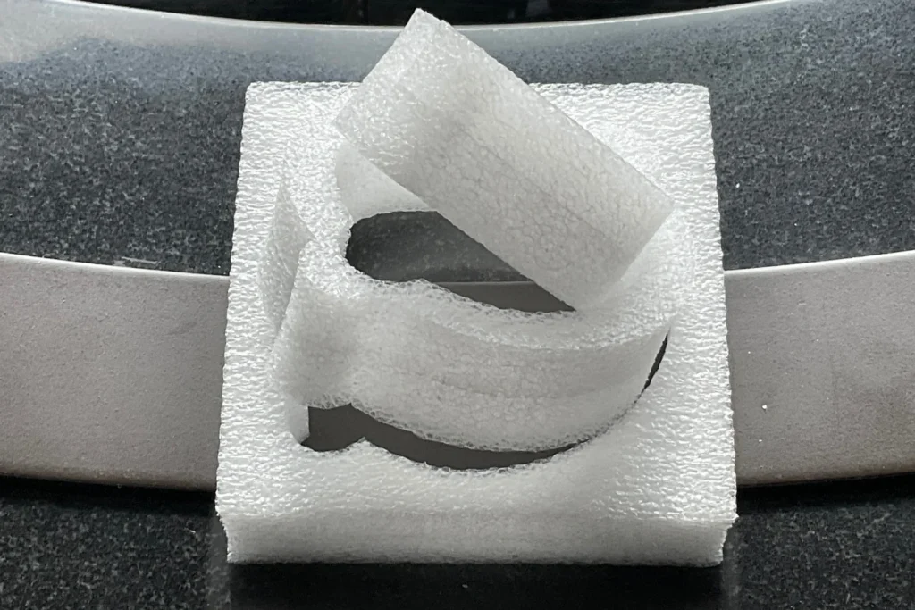A piece of white EPE foam packaging with a circular cutout and a flap folded over the top.