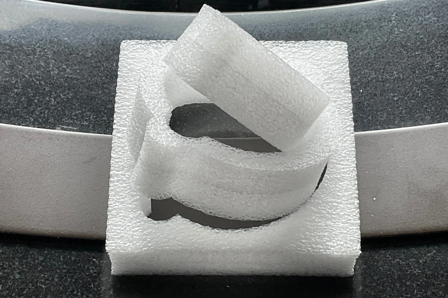 A piece of white EPE foam packaging with a circular cutout and a flap folded over the top.
