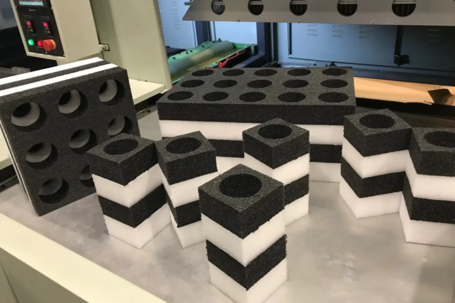 Various foam packaging samples, including rectangular blocks, cylinders, and cubes with different heights and patterns, displayed on a table.
