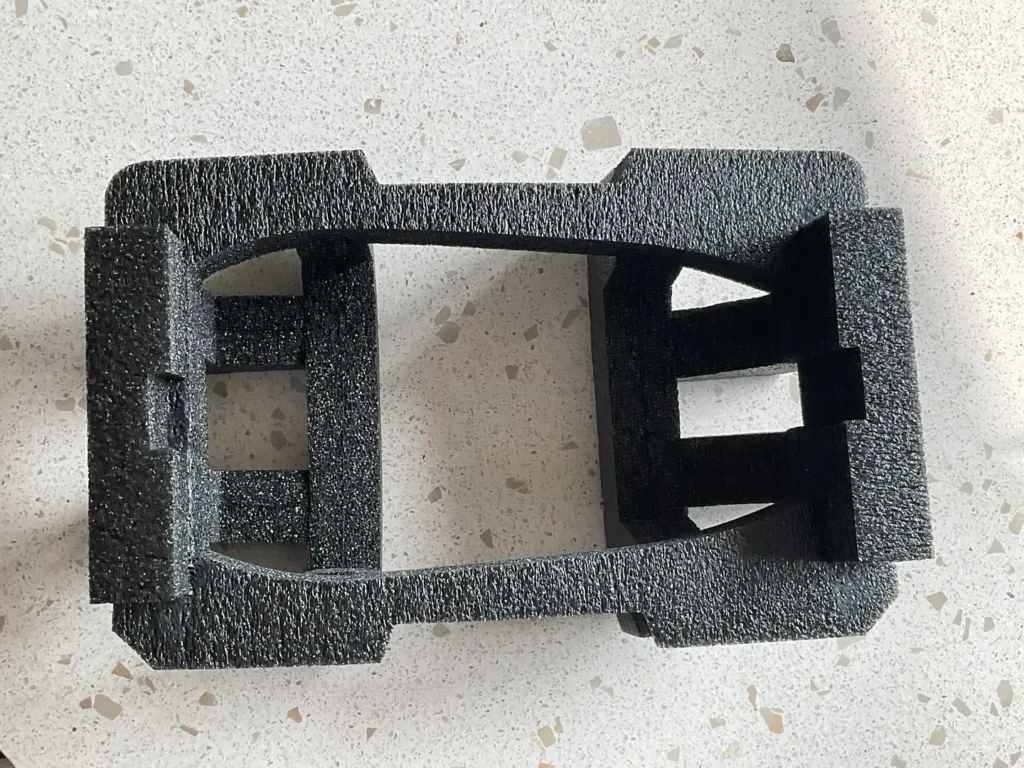 Black foam packaging insert with cutouts, placed on a light speckled surface.